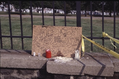 Cardboard sign on a stone wall reading America we Need to Stand Together.