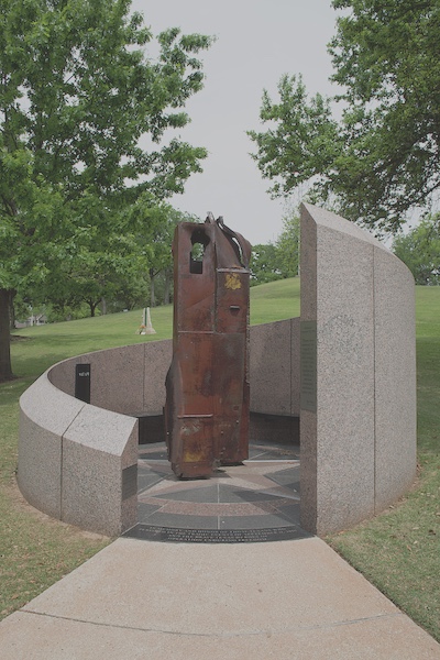 A piece of mangled and rusted steel from the World Trade center stands and a wall of granite encircles it. Upon entering the small space with the beam, from left to right the granite wall gets increasingly taller. Informational panels and memorial notes are placed at the entrance and along the wall.