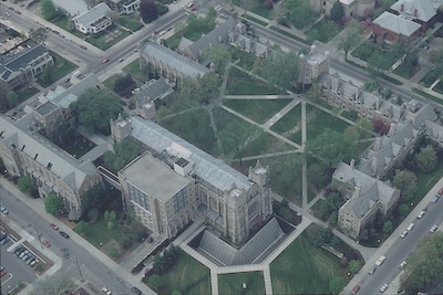 Outdoor aerial view of large stone buildings and green areas with trees. 