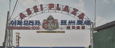 Sign over the entrance to Assi plaza where there is an Asian grocery store as well as a Korean and Chinese specialty store. The sign includes Chinese, English, and Korean writing.