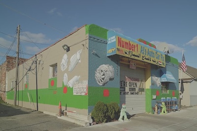 A shop called Number 1 Al's Auto Care Fix (english and arabic) is painted outside with pictures of different car parts