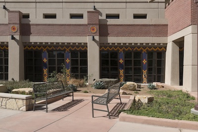 Outside of a building. Two benches face each other outside the building on a concrete path.