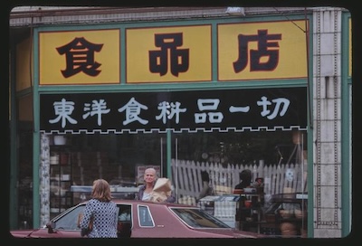 Store front with Chinese characters. Porcelain cups can be see in the window. In the foreground 2 women get into a car.