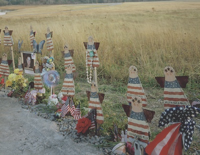 Handmade wooden angels painted with the American flag design. Each is labeled with the name of a passenger from flight 93 who did not survive. Some of the angels are accompanied with photos or sentimental items.