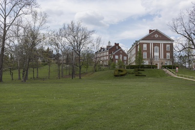 Two brick buildings on a hill just beyond an open grassy field.