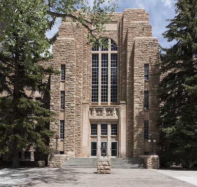 Tall brown stone or brick building with tall paned windows.