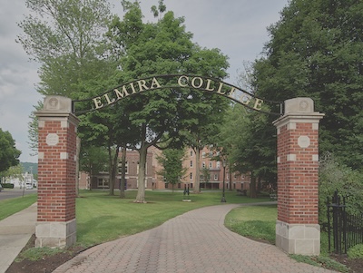 Outside, two brick columns line either side of a brick path. The columns are connected by an arched sign reading Elmira College