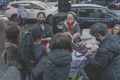 A small group of Filipino women sell headbands and other goods at their booth on a street in New York City