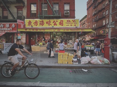 People walk past the GV Trading store on the corner of a street in Chinatown. Someone rides theirbike past