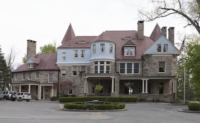 The bottom half of the house is stone and the top half is painted blue with a red roof and a few short turrets.