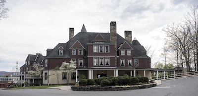 Three story dark brick home with three chimneys and a turret.