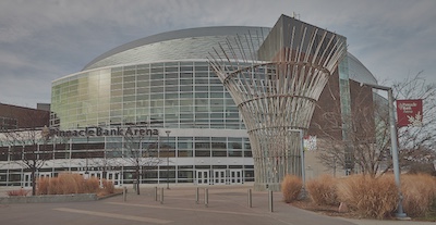 Sculpture in front of a building with tall pieces of metal placed in a circle that bend outwards at the top.