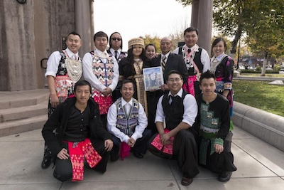 A group of 12 people organized in two lines, the frontline kneeling and the back line standing behind. Participants are wearing traditional clothing. 