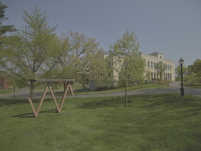 A large two story building on the corner of two paved roads. Lots of open green space in the foreground.