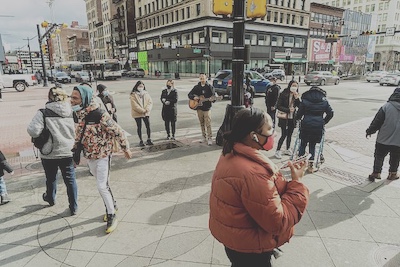 At the corner of Broad street and Market Street in Newark, New Jersey a small group of Korean musicians perform for the public. They stand next to the crosswalk lights and one of them plays a guitar.