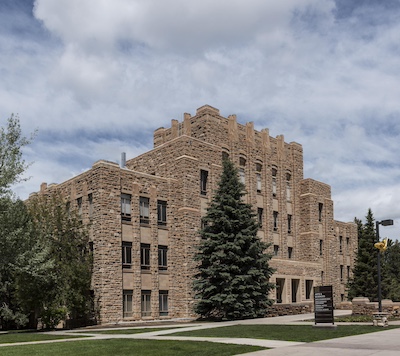 Tall brown building with four floors and windows. The center of the building is the tallest and the height of it decreases to each side.