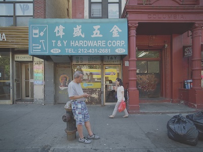 A man lens on a fire hydrant in front of a store in China Town. A woman walks behind him. 