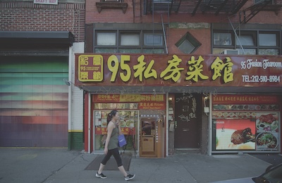 A woman walks past a store-front building in China Town carrying a bag