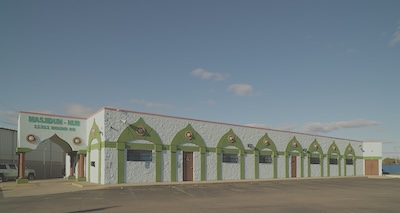 One-story white building with a "Masjidun-Nur" sign and green minaret designs.