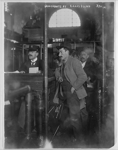 "Male Immigrants at Ellis Island." A man stands in line waiting while another man who works at Ellis Island handles his paperwork.