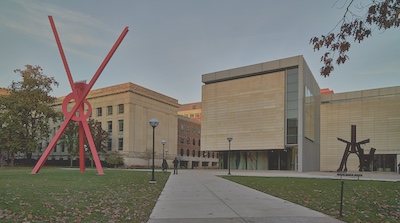 Large abstract sculpture is on a green lawn next to a sidewalk.