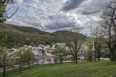 Photo of Potomac State College campus as it sits in a valley. Just behind the campus is a forested mountain. This photo is taken from a hill on the other side of the valley.