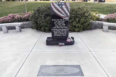 Black stone memorial resembling a large headstone that reads "If but one life be saved and one soul be comforted... all gave some some gave all and some still give. In honor and memory of all those who lost their lives in the rescue efforts of September, 11, 2001." The stone is painted to look like an American flag is draped over the top.