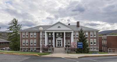 Three story brick building with four columns at the entrance and two chimneys on the roof.