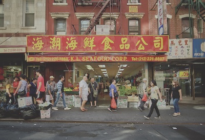 Pedestrians walk in front of a store with a red awning reading K.L. Seafood Corps in Chinatown