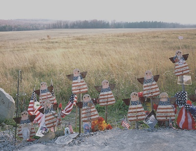 Handmade wooden angels painted with the American flag design. Each is labeled with the name of a passenger from flight 93 who did not survive. Some of the angels are accompanied with photos or sentimental items.