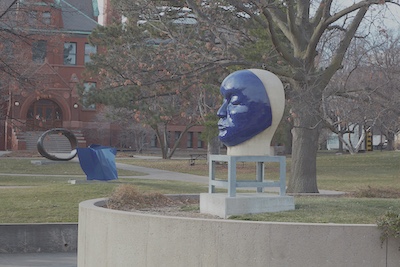 Large abstract sculpture on a lawn of a head with no hair, but a bright blue face.