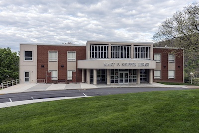 Brick and cement building just beyond a green lawn and a small roadway.