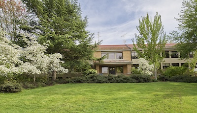 Bright green grass field lined with green and blossoming trees. A brick building sits on the far edge of the field.