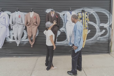 A woman stands points to one of several suits hanging in front of a closed garaged door.