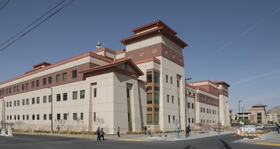 Large four-story sand academic colored building with pedestrians walking by on a paved path. 