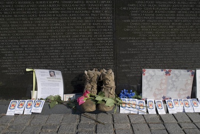 Close up photo of the Vietnam War Memorial in Washington, DC on Veterans day. There are soldier's boots, letters, photos, flowers, and other sentimental items placed in front of the memorial