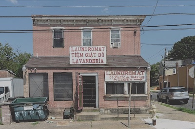 Photo taken in 2023 of a brick building with two signs on it written in Vietnamese indicating where to enter for pizza or for laundry service.