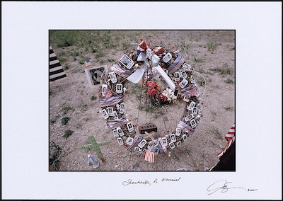 Wreath containing photographs, American flags, flowers, and crosses held up by a stand close to the ground. Shanksville, PA written across the bottom