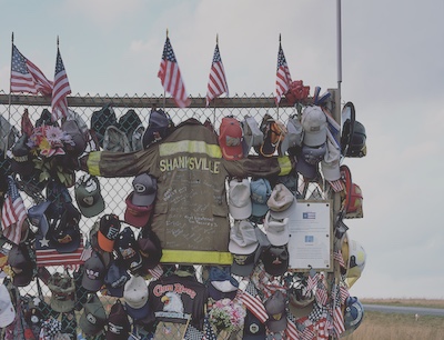 A closer view of memorial gate in Shanksville that shows the firefighter jacket, a number of caps, several firefighter helmets, American flags, and more that have been placed on the fence.