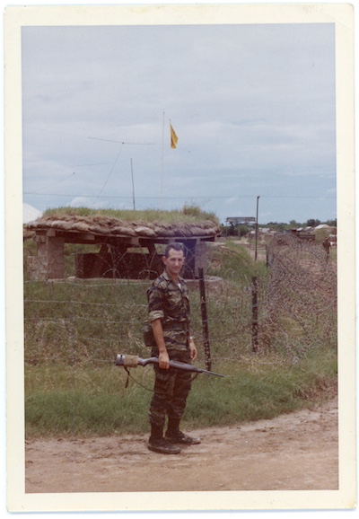 In Vietnam in the 1960s. He stands on a dirt road in his marine uniform with a rifle in hand